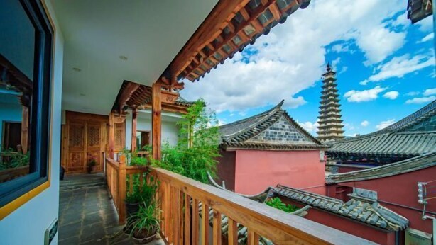 A traditional building with a wooden balcony, a pagoda in the background, and a clear sky. - Huachengju View Guesthouse (Jianshui)