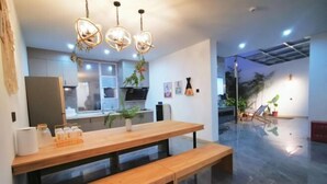 A modern kitchen with a wooden dining table, bench, pendant lights, and a view of the living area. - Huachengju View Guesthouse (Jianshui)