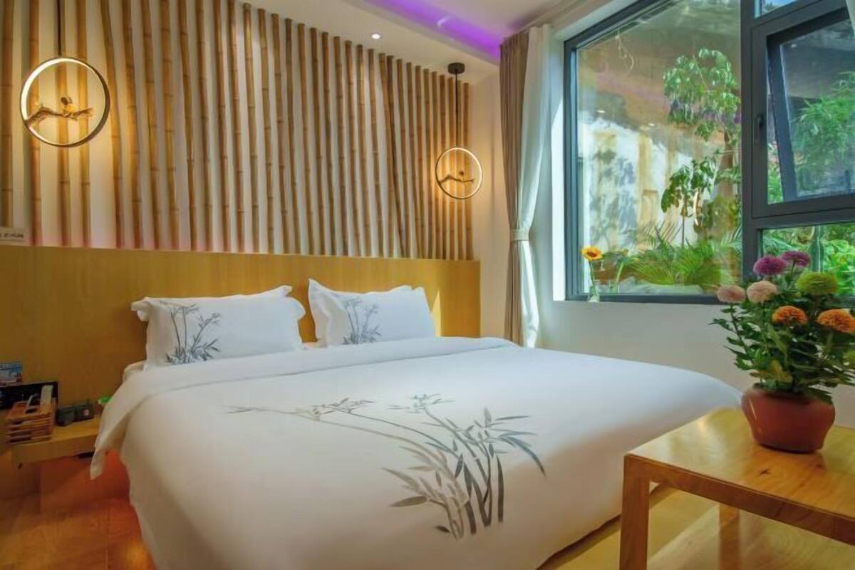 A bed with a white bedspread, a wooden headboard, and a window with plants.