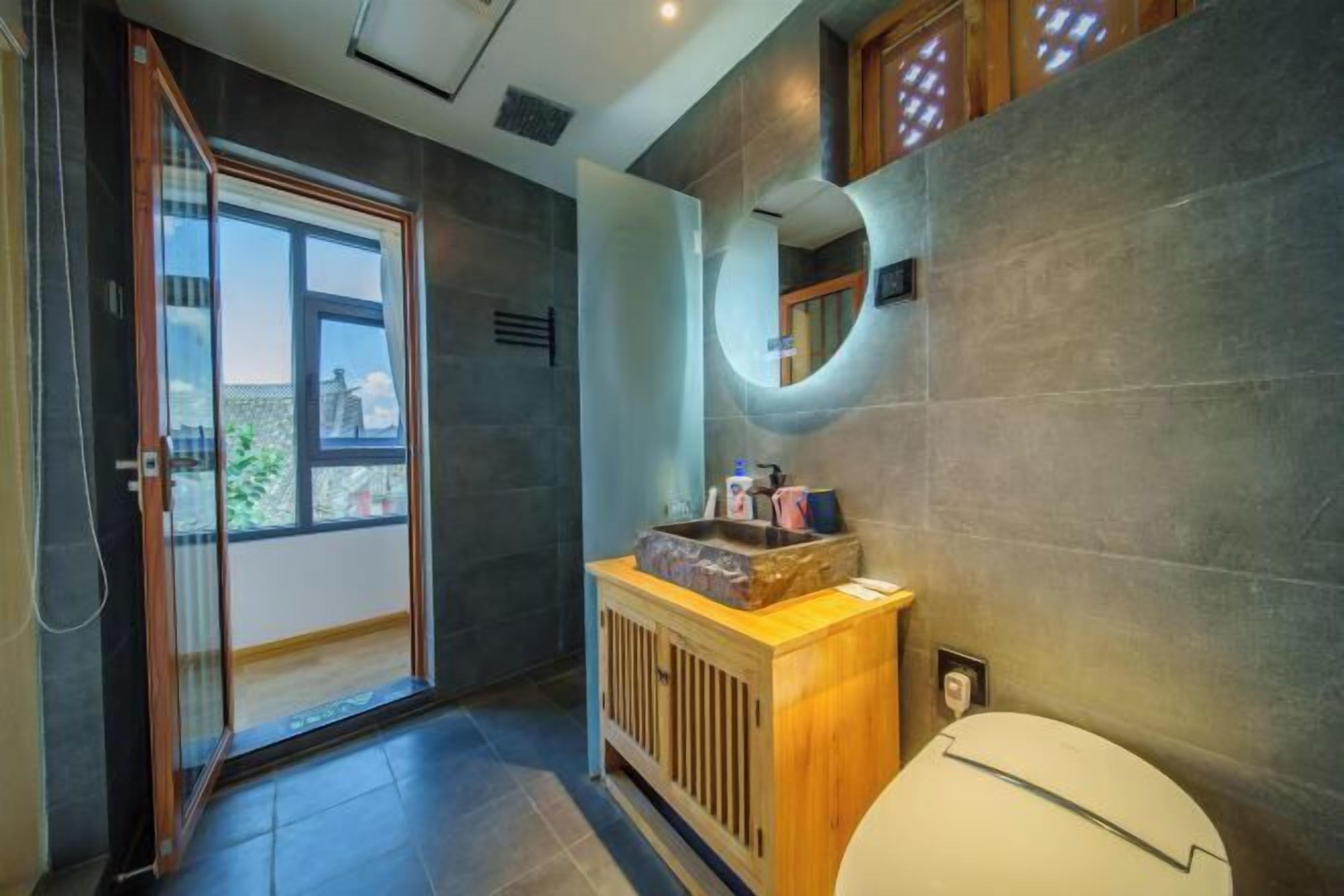 Un baño moderno con inodoro, tocador de madera, lavamanos y un espejo grande.