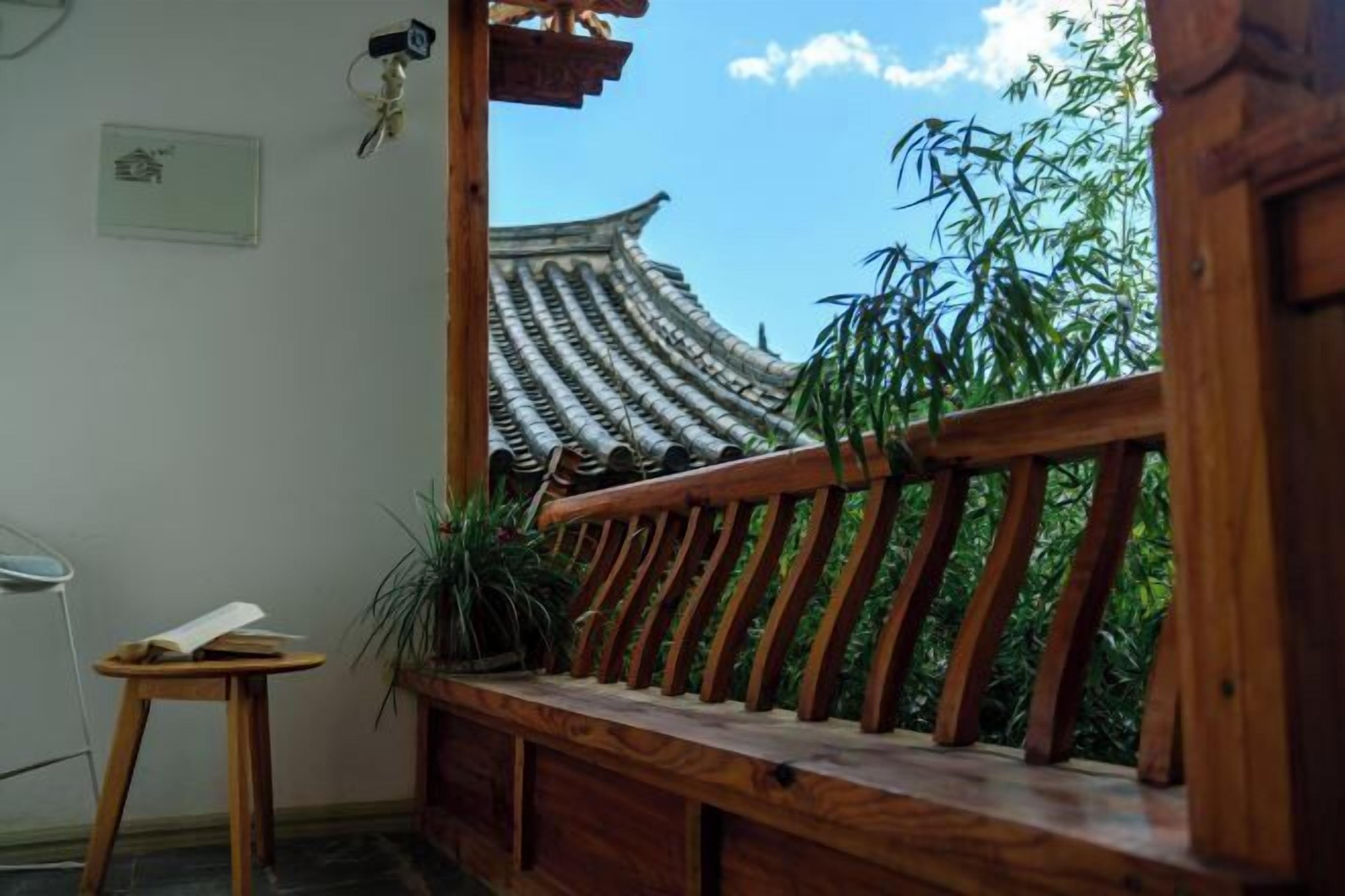 A traditional wooden balcony with a view of a pagoda-style roof and bamboo plants.