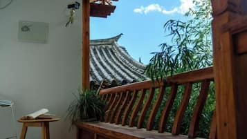 A traditional wooden balcony with a view of a pagoda-style roof and bamboo plants.