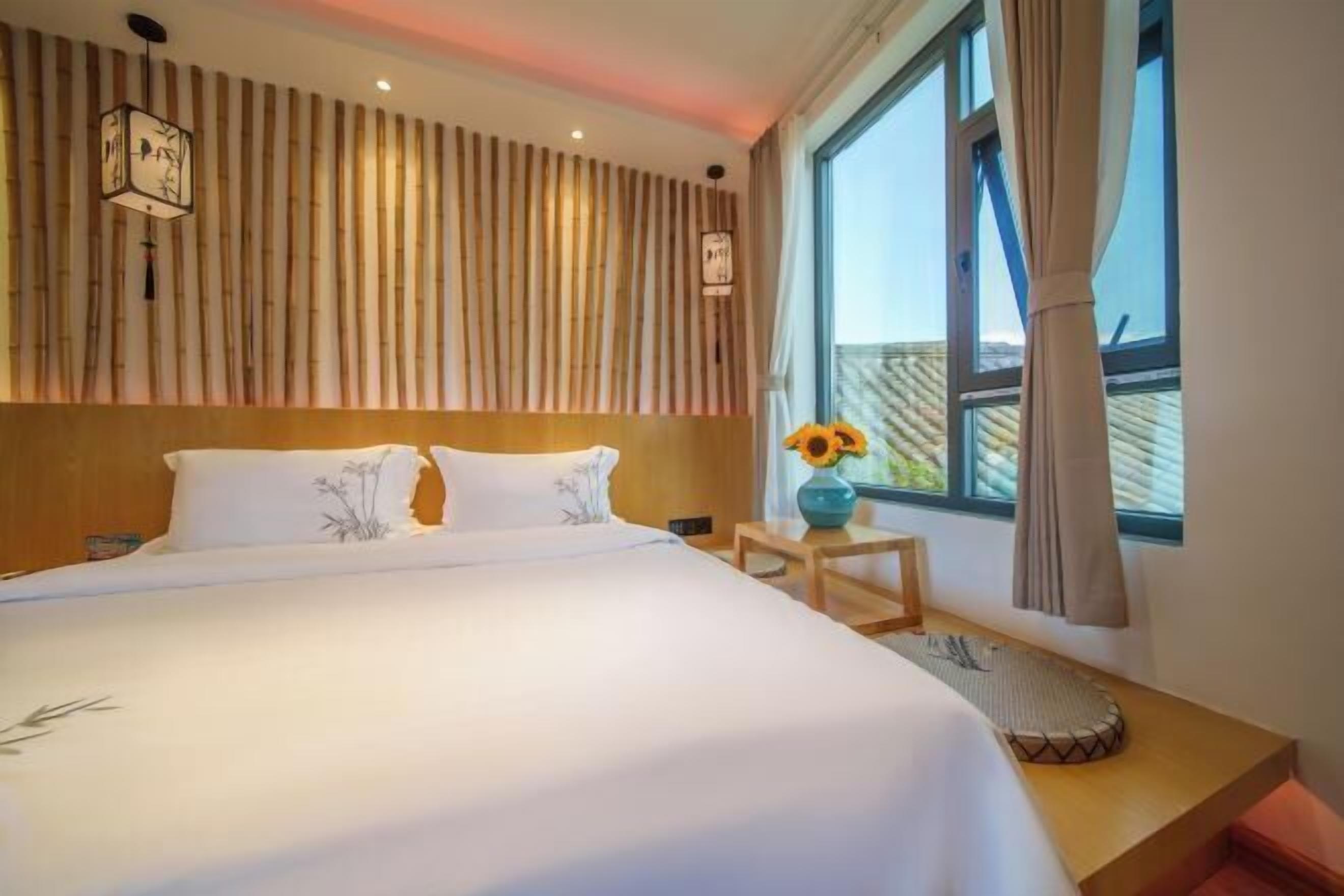 A hotel room with a large bed, a wooden headboard, a small table with a vase of sunflowers, and a window with curtains.