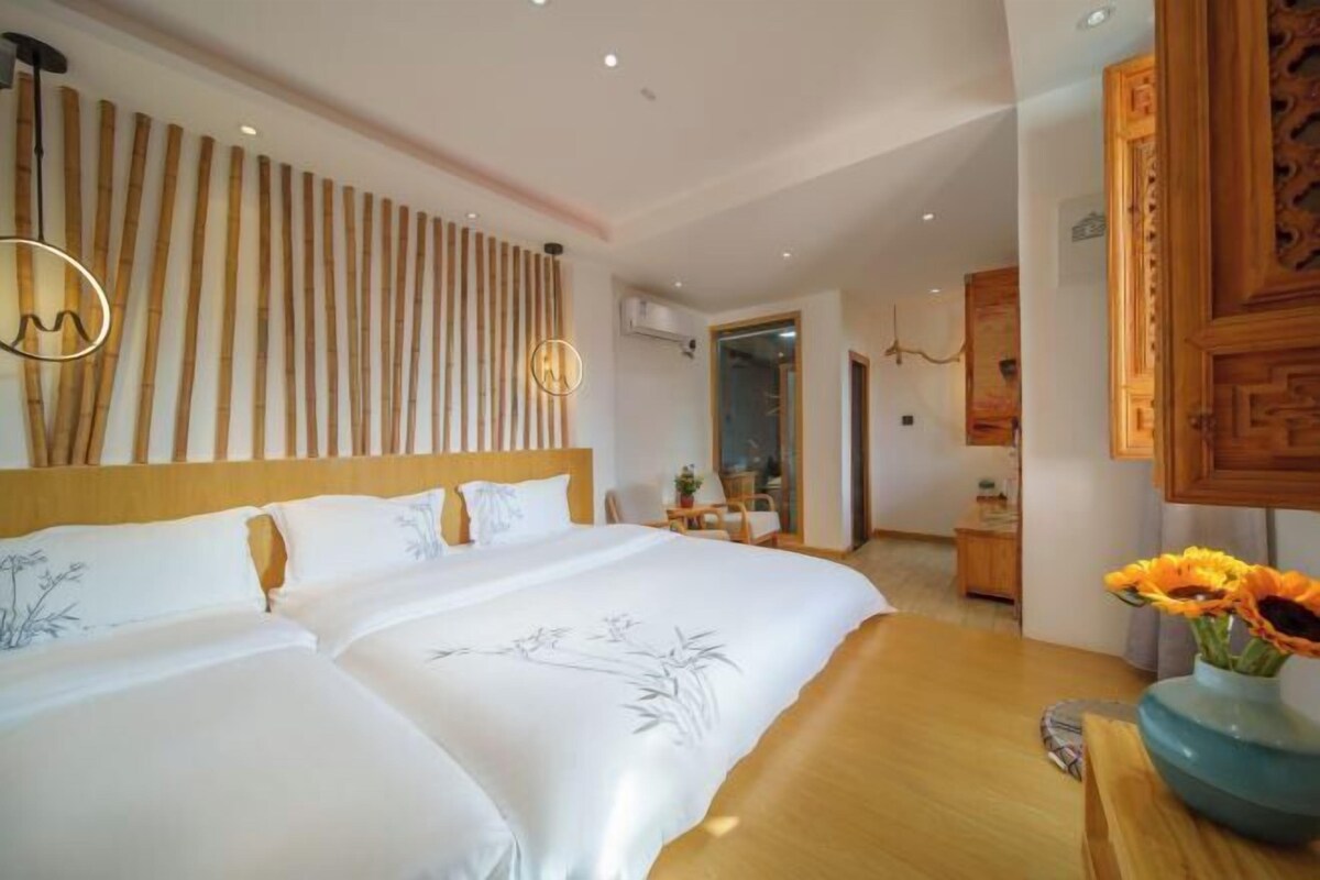 A hotel room with a large bed, a wooden headboard, a wall with vertical wooden slats, a small table with a vase of flowers, and a wooden cabinet.