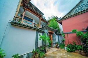 Un patio tradicional con un muro rojo, un edificio blanco con balcón y plantas en macetas.