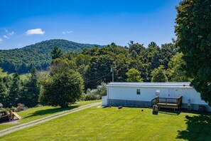 A single-story white building with a metal roof, surrounded by a grassy yard and trees. - Pet friendly, hdtv°Fireplace°Netflix°Backyard (Deep gap)