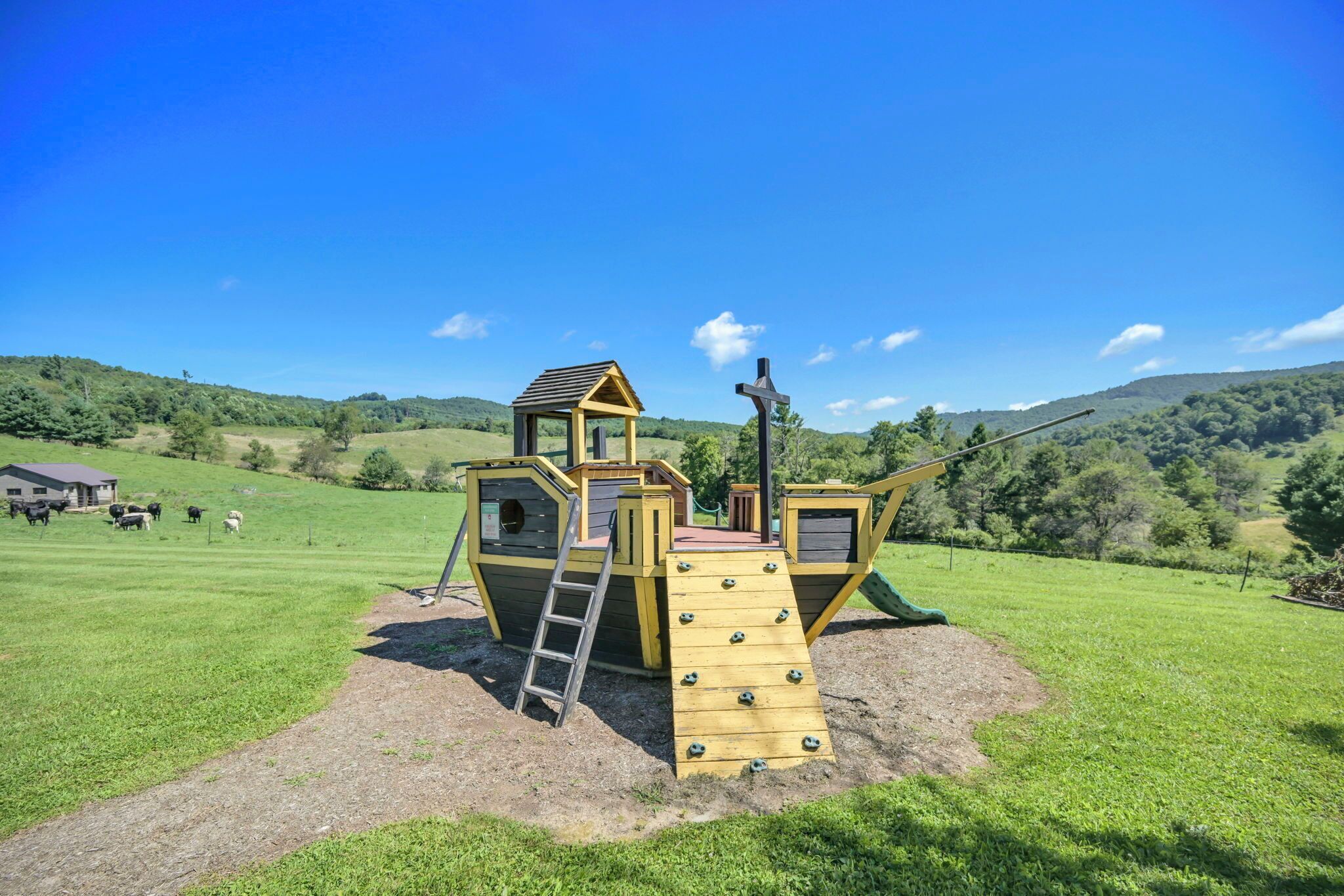 A playground with a climbing structure and a slide, set in a grassy field with a clear sky.