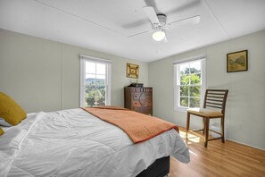 A bedroom with a bed, a chair, a dresser, and two windows with views.