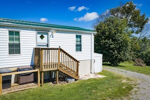 A mobile home with a wooden deck, a small outdoor trash bin, and a covered area for storage.