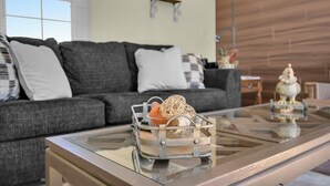 Ein modernes Wohnzimmer mit einem Glastisch, einem grauen Sofa und Dekorationselementen.