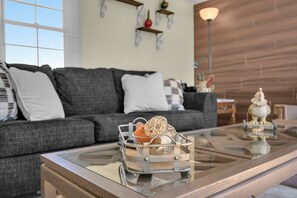 Ein modernes Wohnzimmer mit einem Glastisch, einem grauen Sofa und Dekorationselementen.