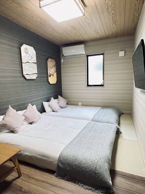 A bedroom with two beds, a wooden ceiling, a skylight, a mounted air conditioner, and a window. - Tabitime tengachaya  (Osaka)