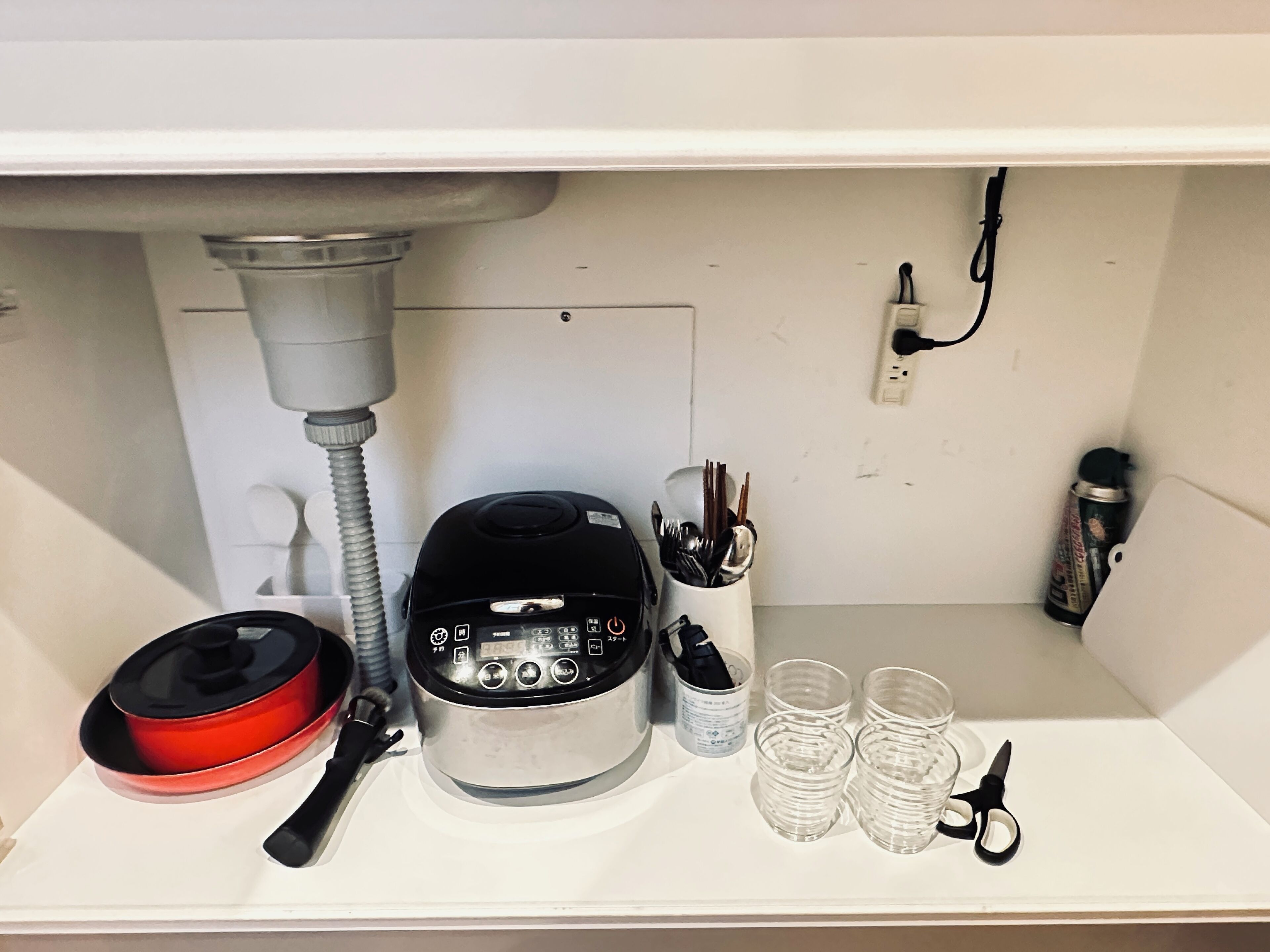 A kitchen shelf with a rice cooker, a red pot, a set of chopsticks, a can of spray paint, and a pair of scissors.