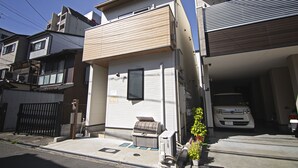 A residential building with a garage, a small outdoor seating area, and a vehicle parked inside. - Tabitime tengachaya  (Osaka)