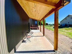 Ett takförsett utomhusområde med ett betonggolv, en träpergola och utsikt över ett hus i bakgrunden.