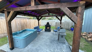 A covered outdoor patio with a hot tub, two chairs, a grill, and a fireplace. - Pool Table, Hot Tub! 5 bedroom, 3 bath, 5 min to Cal Poly or Old Town. (Eureka)