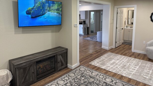 A modern living room with a flat-screen TV, a fireplace, and a hallway leading to a kitchen and bathroom. - Pool Table, Hot Tub! 5 bedroom, 3 bath, 5 min to Cal Poly or Old Town. (Eureka)