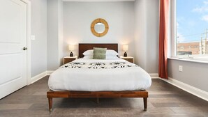 A bedroom with a large bed, a round mirror above the bed, two bedside lamps, and a window with curtains. - ★ HostWise Stays ★ Skyline Views | Rooftop Deck & Gourmet Kitchen (Pittsburgh)