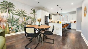 A modern kitchen with white cabinets, a central island, and a dining area with a wooden table and chairs. - ★ HostWise Stays ★ Skyline Views | Rooftop Deck & Gourmet Kitchen (Pittsburgh)