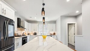 A modern kitchen with white cabinetry, a large marble island, and a stainless steel refrigerator. - ★ HostWise Stays ★ Skyline Views | Rooftop Deck & Gourmet Kitchen (Pittsburgh)