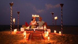A couple dining on a beach at night with a table set with candles and a rug. - Ozaki Desert Camp Jaisalmer (Jaisalmer)