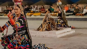 A person with a flame on their head, seated on a white platform, with a crowd in the background. - Ozaki Desert Camp Jaisalmer (Jaisalmer)