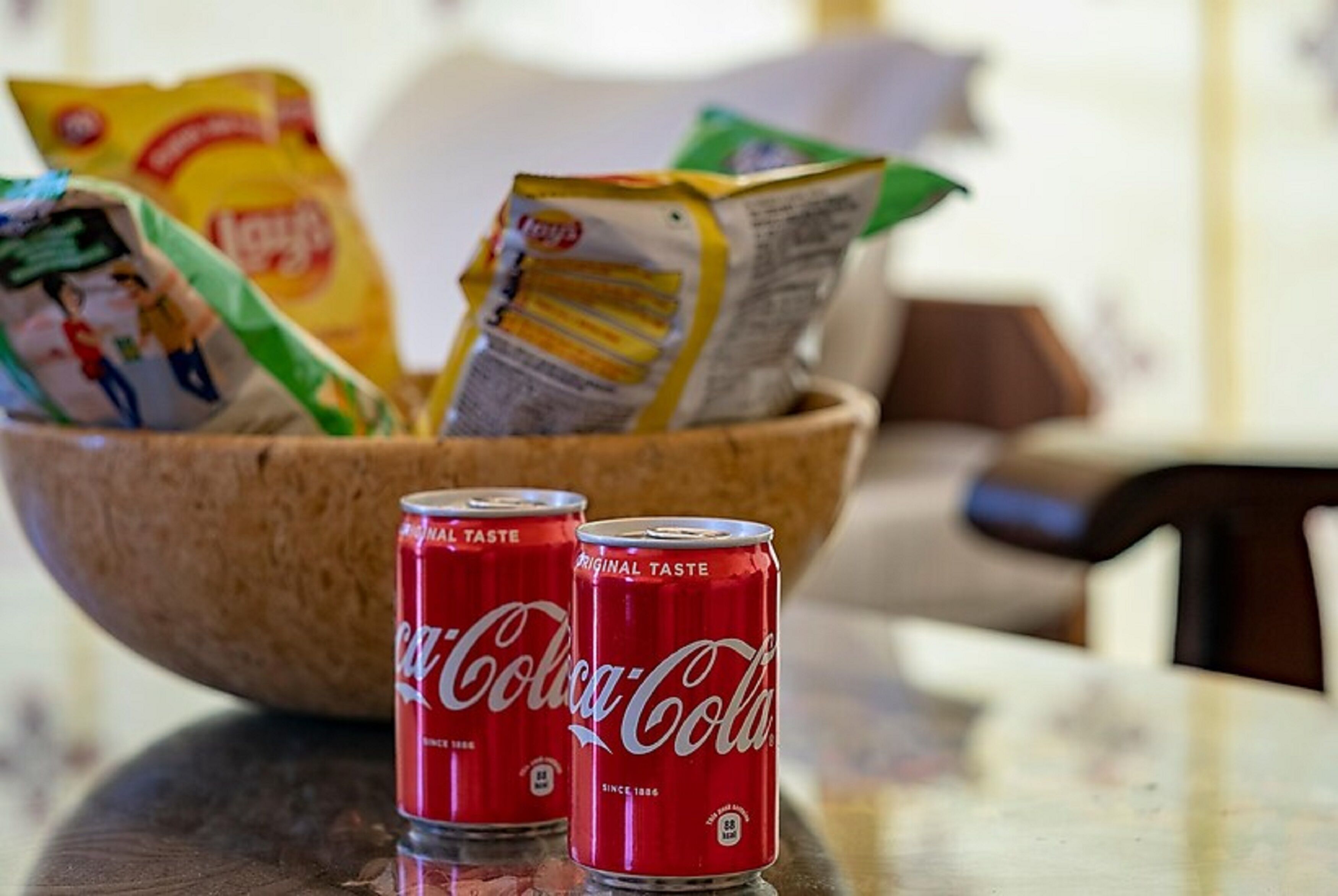 Kaksi Coca-Cola-tölkkiä kulhossa, jossa on myös erilaisia pikkupaketteja naposteltavaksi.