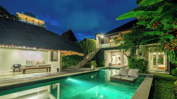 A modern pool area with a thatched-roof structure, a staircase, and a well-lit lounge area.
