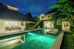 Ein moderner Poolbereich mit einer strohgedeckten Struktur, einer Treppe und einer gut beleuchteten Lounge-Ecke.