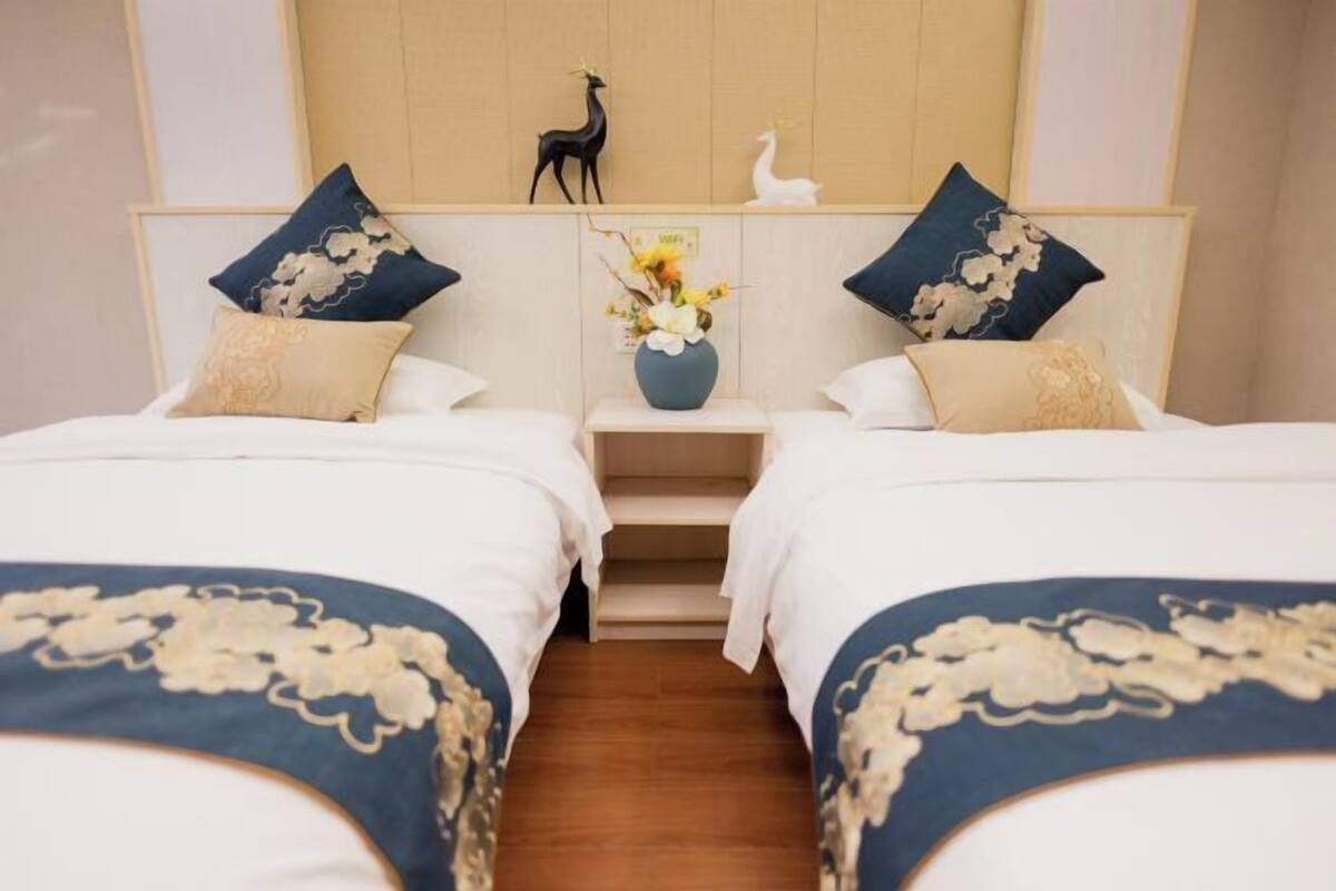 A hotel room with two beds, a nightstand with a vase of flowers, and decorative items on the headboard.