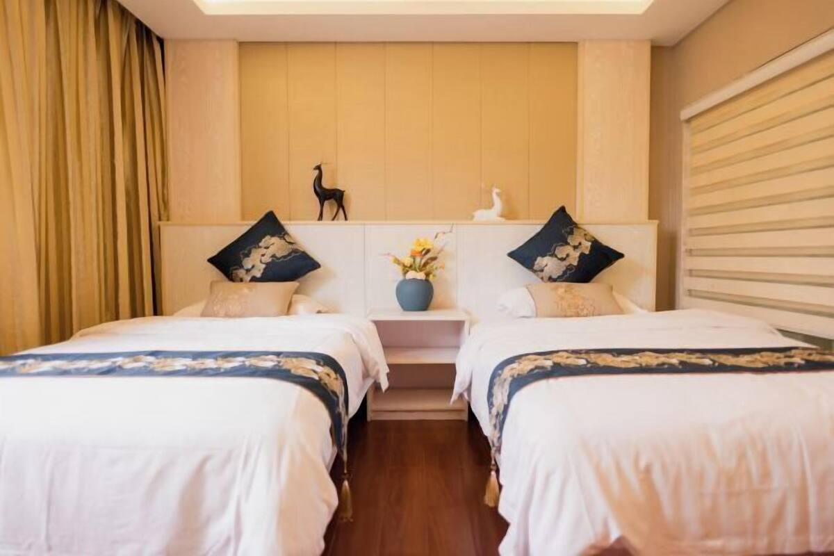 A hotel room with two beds, a wooden headboard, a vase with flowers, and a small shelf with decorative items.