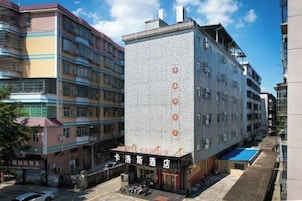 Un edificio de varios pisos con una entrada destacada, un estacionamiento visible y construcciones más pequeñas adyacentes.