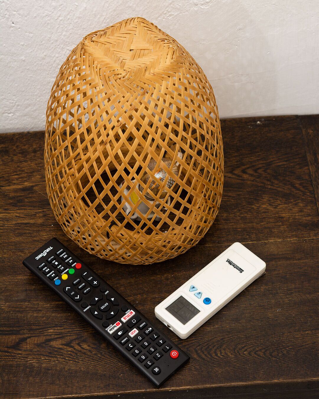 Un panier en osier, une télécommande noire et un appareil électronique blanc, le tout posé sur une surface en bois.