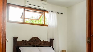 A wooden bed with white and dark bedding in a room with a window and an air conditioning unit. - CASA DE PLAYA FRENTE AL MAR CON JACUZZI  (Cartagena)
