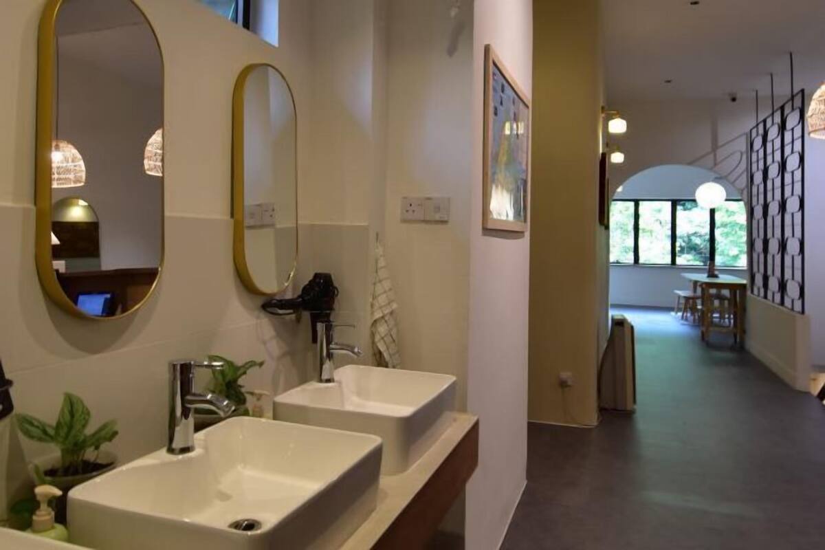 A modern bathroom with two sinks, a large mirror, and a view into the adjacent dining area.