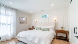 A bedroom with a large bed, a nightstand, a dresser, and a window with curtains. - Reno Dream Cottage: Delightful 2-Bedroom Sanctuary (Reno)