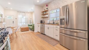 A modern kitchen with stainless steel appliances, wooden flooring, and a green sofa in the living area. - Reno Dream Cottage: Delightful 2-Bedroom Sanctuary (Reno)