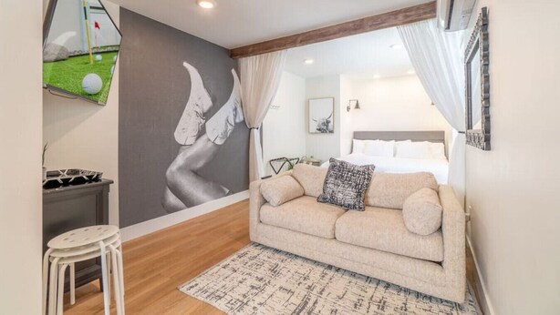 Un dormitorio moderno con una cama grande, un sofá, una mesita y un televisor montado en la pared.