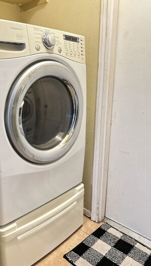 A front-loading washing machine in a laundry room with a checkered floor mat.