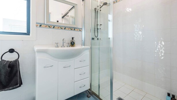 A bathroom with a glass-enclosed shower, a white sink with a mirror above it, and a towel rack with a towel.