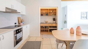 Une cuisine moderne avec des meubles blancs, un four encastré et un coin repas comprenant une table et des chaises en bois.