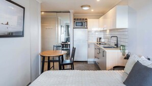 Une chambre d’hôtel de taille réduite, comprenant un lit, une petite table à manger, un coin cuisine et une salle de bain.