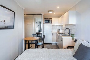A compact hotel room with a bed, a small dining table, a kitchenette, and a bathroom. - Yamba Views Studio (Yamba)