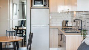 Une cuisine compacte équipée d’un four à micro-ondes, d’un réfrigérateur et d’un évier. On y trouve une table à manger avec des chaises et une petite fenêtre.