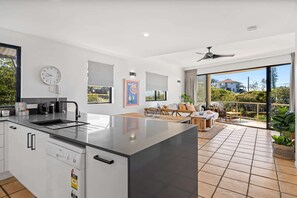 Une cuisine moderne dotée d’un grand îlot central, d’un coin repas offrant une vue agréable et d’un balcon agrémenté de plantes.