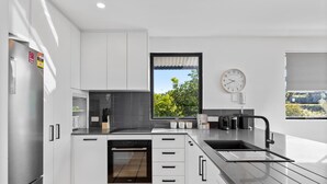 A modern kitchen with white cabinets, a built-in oven, a large window, and a clock on the wall. - Pristine 2-Bed Apartment with Pool and Balcony (Sunrise Beach)