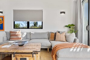 Un salon moderne avec un canapé, une table basse et une vue sur l’extérieur par une fenêtre.