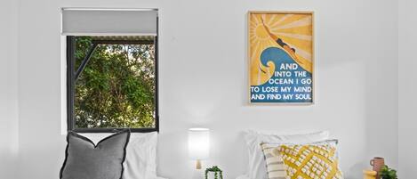 Ein Schlafzimmer mit zwei Betten, einem Fenster mit Blick auf Bäume, einer Wand mit einem motivierenden Zitat, einer Nachttischlampe und einem kleinen Tisch mit einer Pflanze.