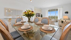 A dining area with a glass table, white plates, and a vase of flowers.