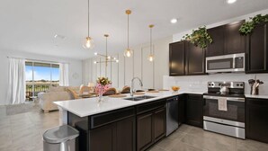 A modern kitchen with dark cabinets, stainless steel appliances, and pendant lighting.